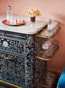 Tray with bottle and glasses on table, alongside various crystal glasses on side rack.