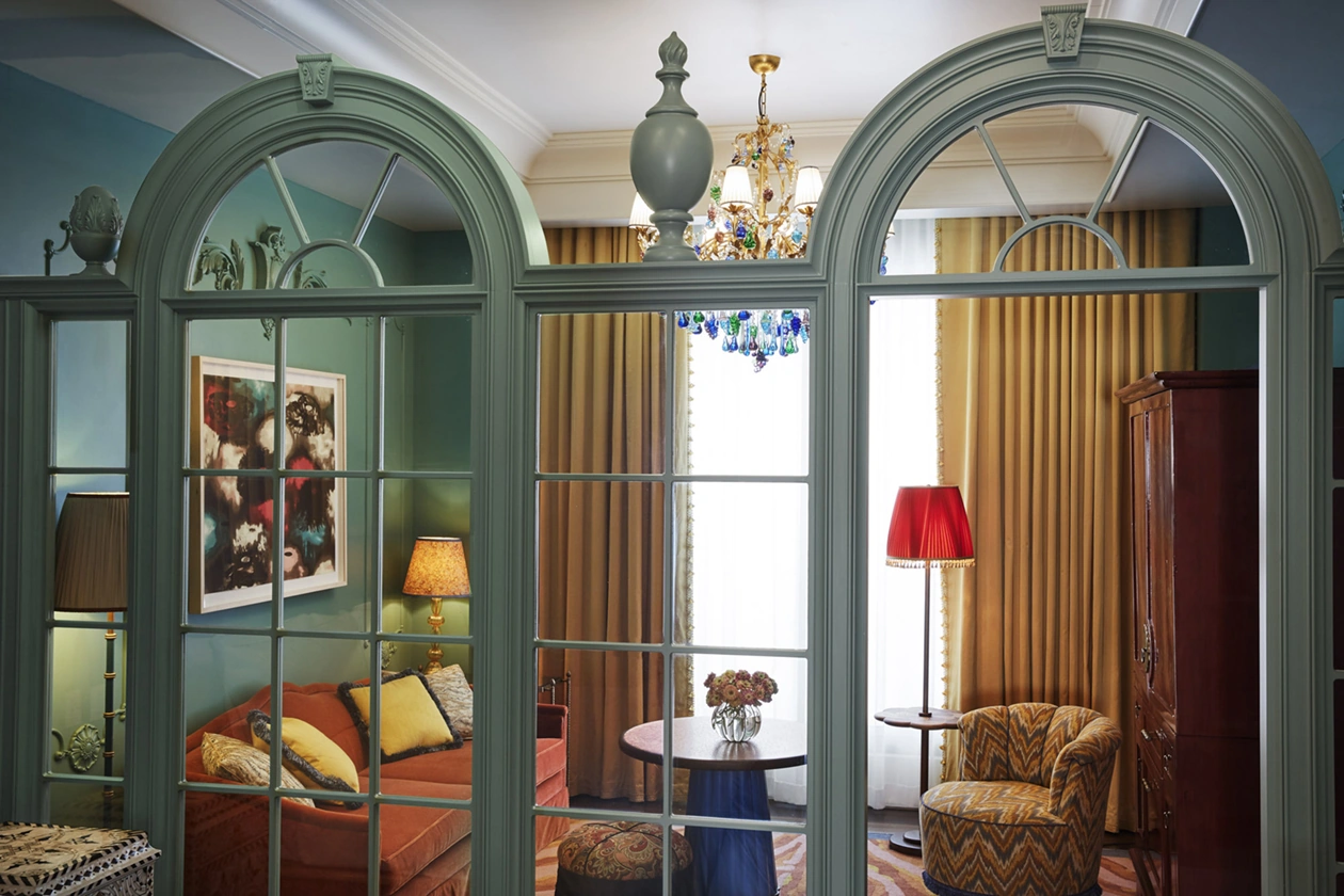 A living area is seen through a transparent glass frame, featuring a sofa set, coffee table, and a portrait on the left wall.