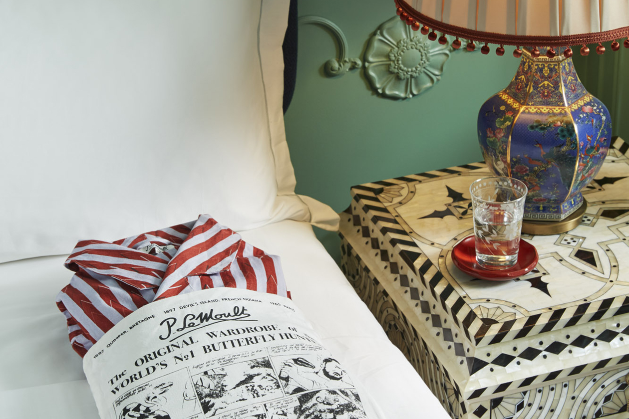 Neatly folded shirt in a paper bag on the bed, antique lamp and water glass on the side table.