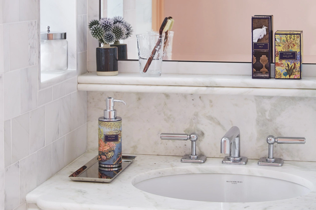A pristine white marble washbasin, equipped with handwash and fragrances, enhances a fresh and clean ambiance.
