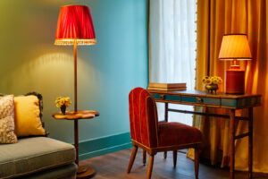 Table with chair, featuring notebooks, night lamp, and a standing lamp alongside the couch.
