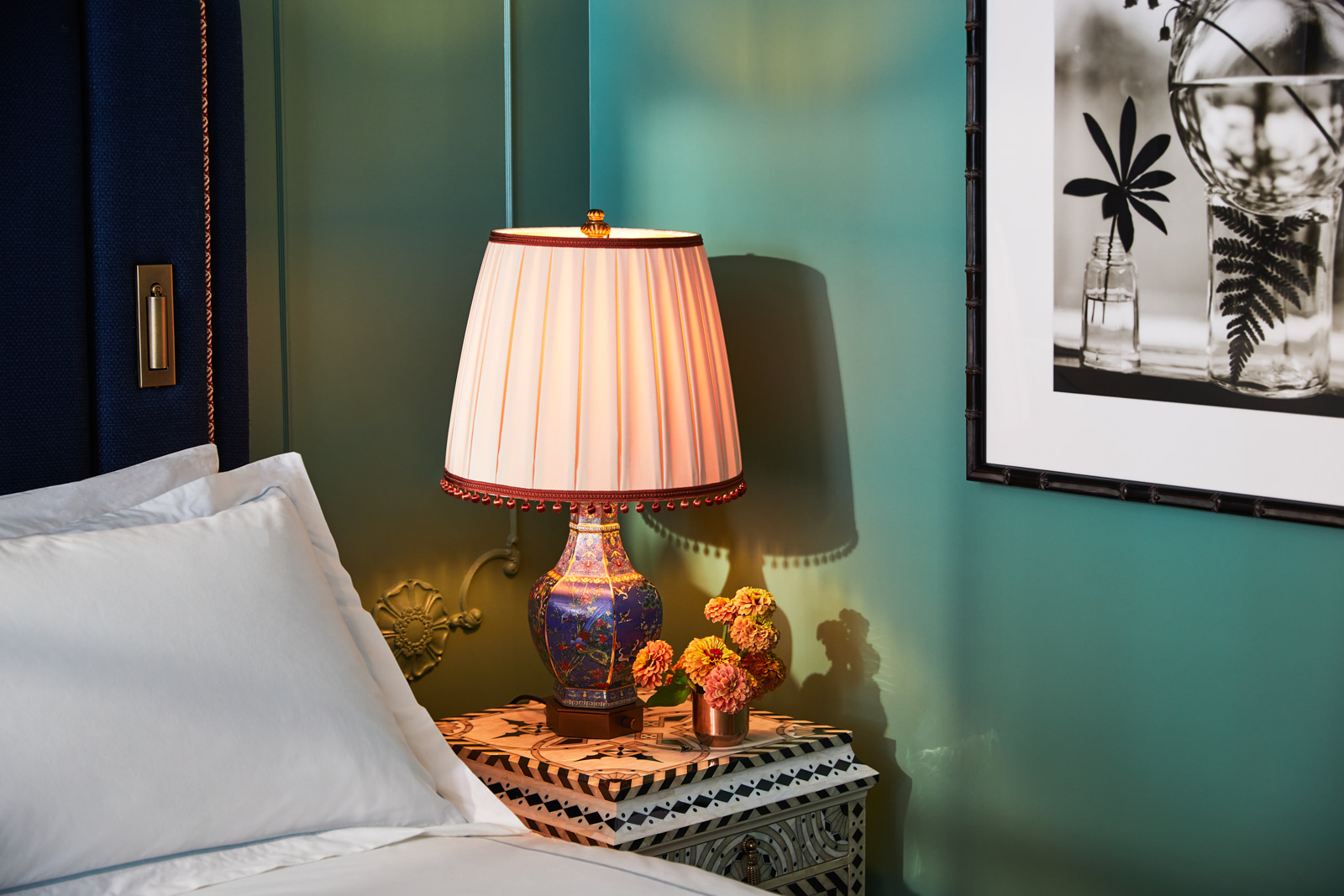 Night lamp and petite vase on bedside table, a portrait hanging on the right wall.