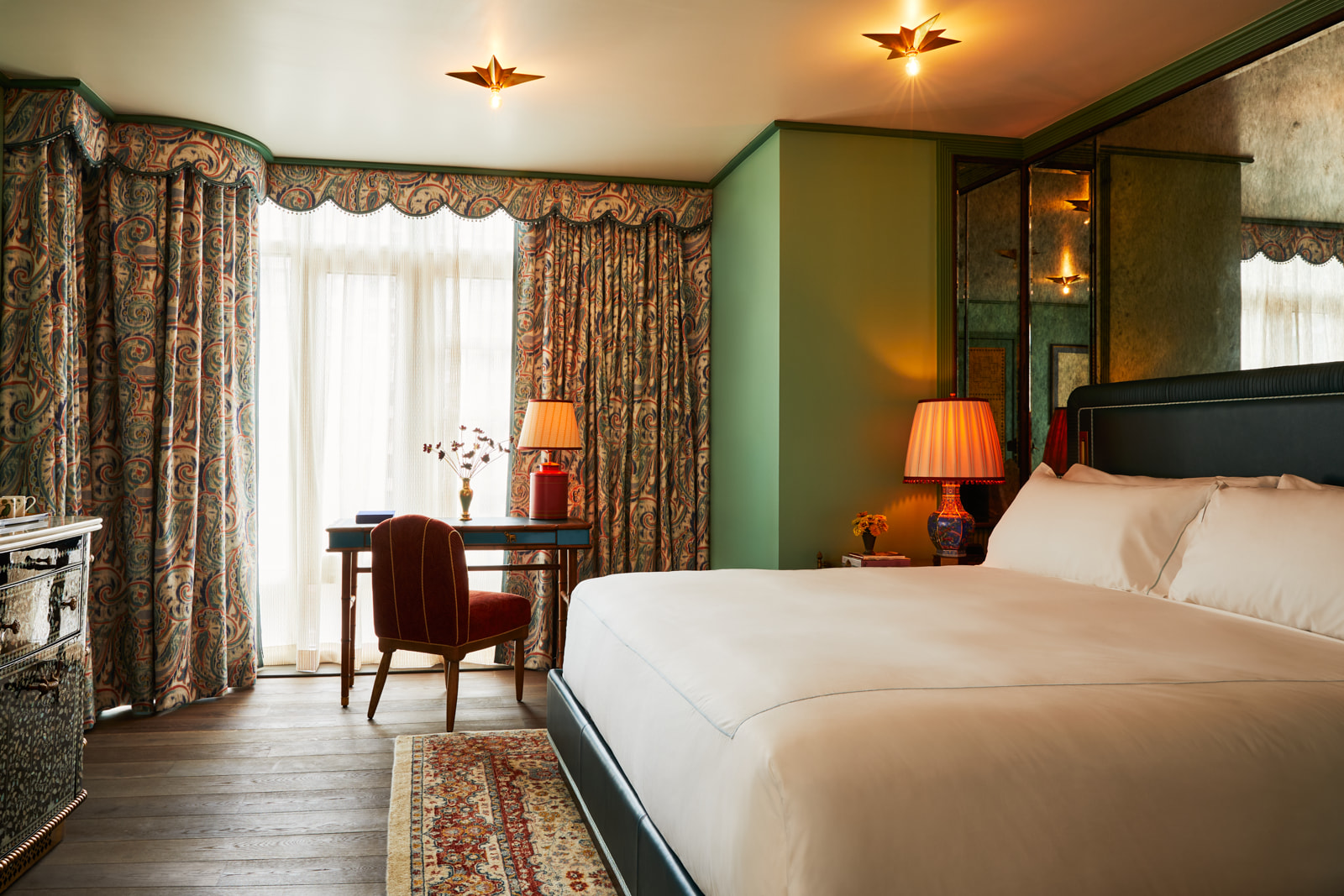 Tastefully arranged bedroom with pristine bed, table with a chair by the window, adorned with golden lighting.