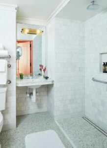 Bathroom with white marble finish, mirror above washbasin, small flower vase on the sink.