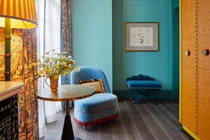 Sofa near window, table with vase, portrait hung on blue wall, forming an inviting ambiance.