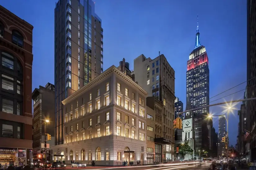 Captured image of The Fifth Avenue Hotel brilliantly illuminated at night, surrounded by towering skyscrapers.