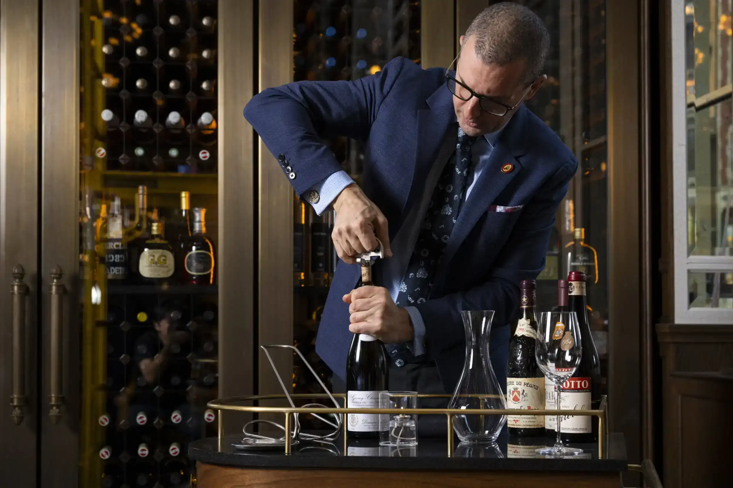 In the bar, a man in a blue suit trying to open a wine bottle.