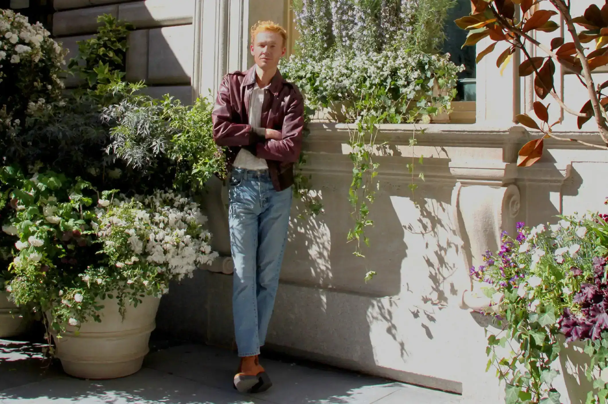A man in a brown jacket poses for a photo beside a large flower pot.