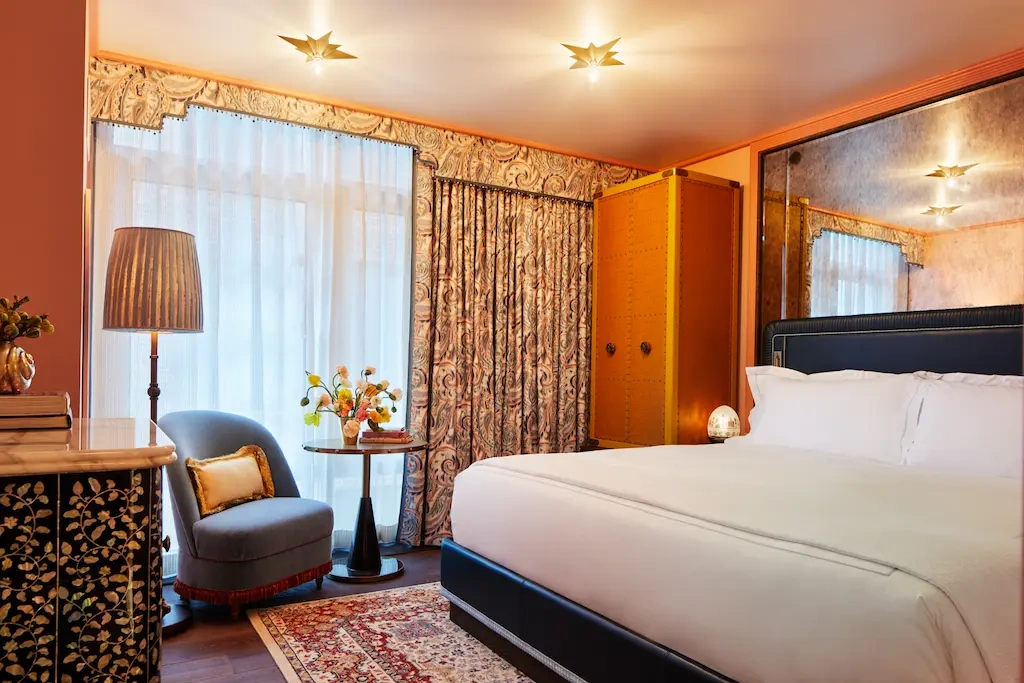 A well-arranged bedroom with a cozy bed, standing lamp, chair, and coffee table by the window.