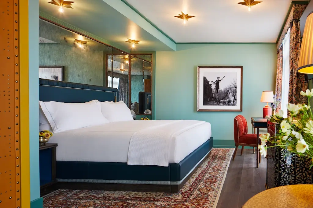 A well-arranged room with a cozy bed and a beautiful portrait on the right wall.