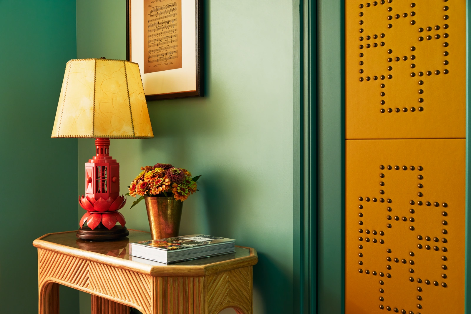 A lamp, flower pot, and notebook are on the table, with a portrait mounted above.
