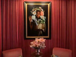 A beautiful lady's portrait mounted on a red-painted wall with a small flower pot in front.