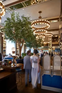 Upscale restaurant interior with chandeliers, central tree, gold accents, and guests dining