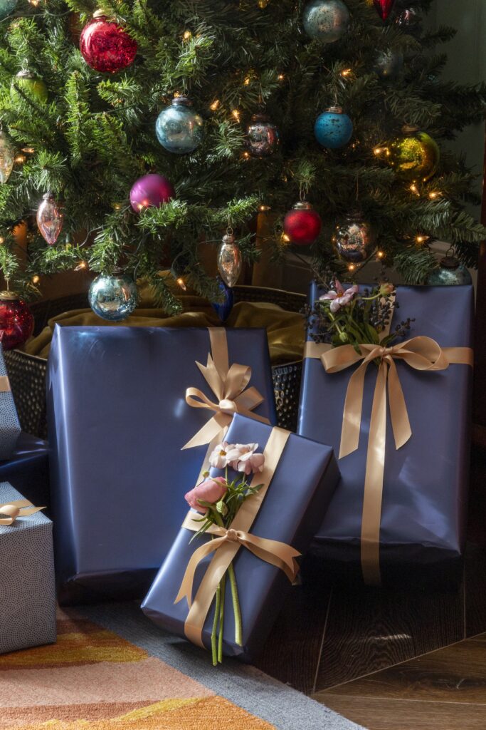 Beautifully wrapped Christmas presents arranged under a festive tree, glowing with warm holiday lights