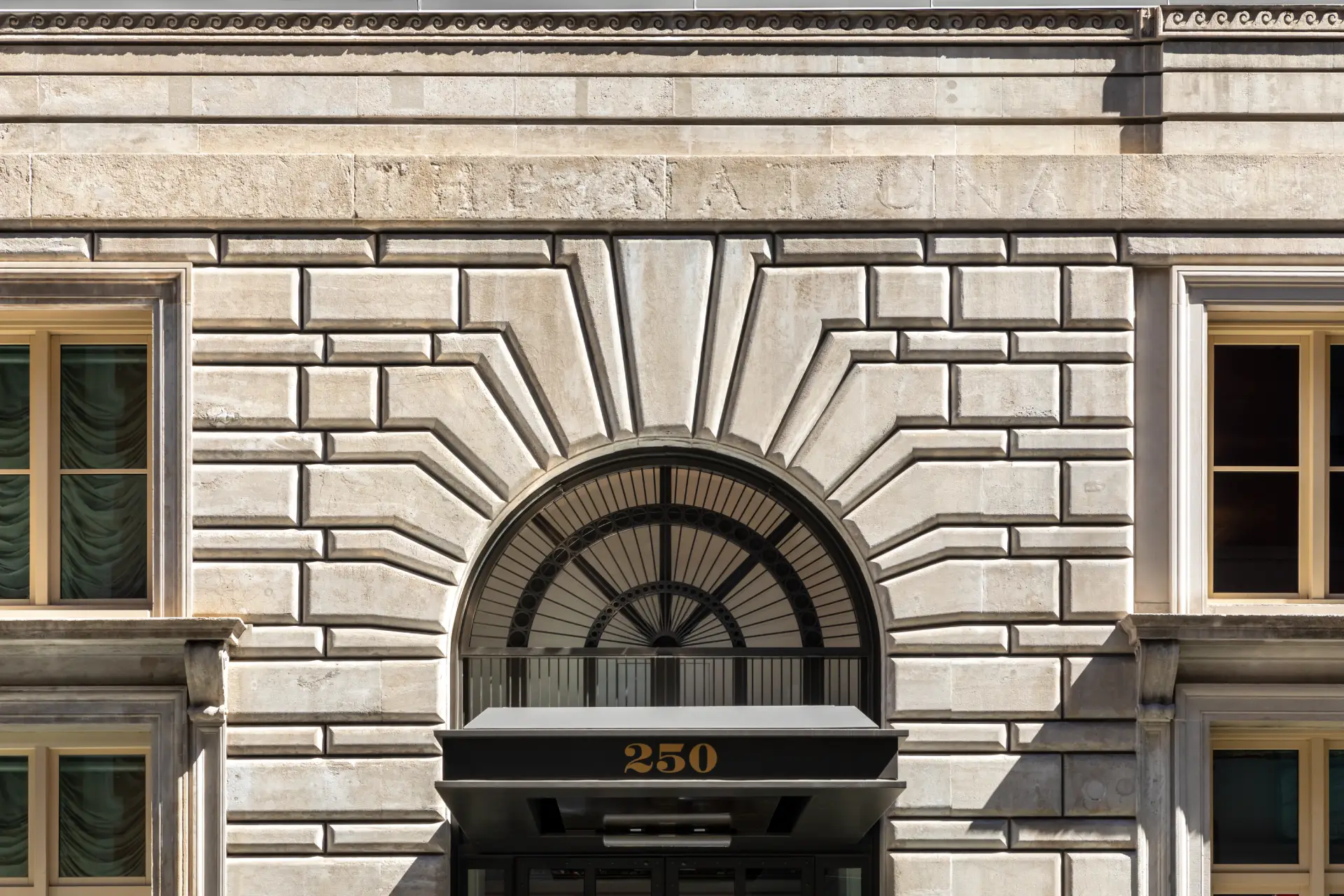 Classical stone facade with arched window, gold "250" on black awning, and symmetrical windows with light-colored frames.