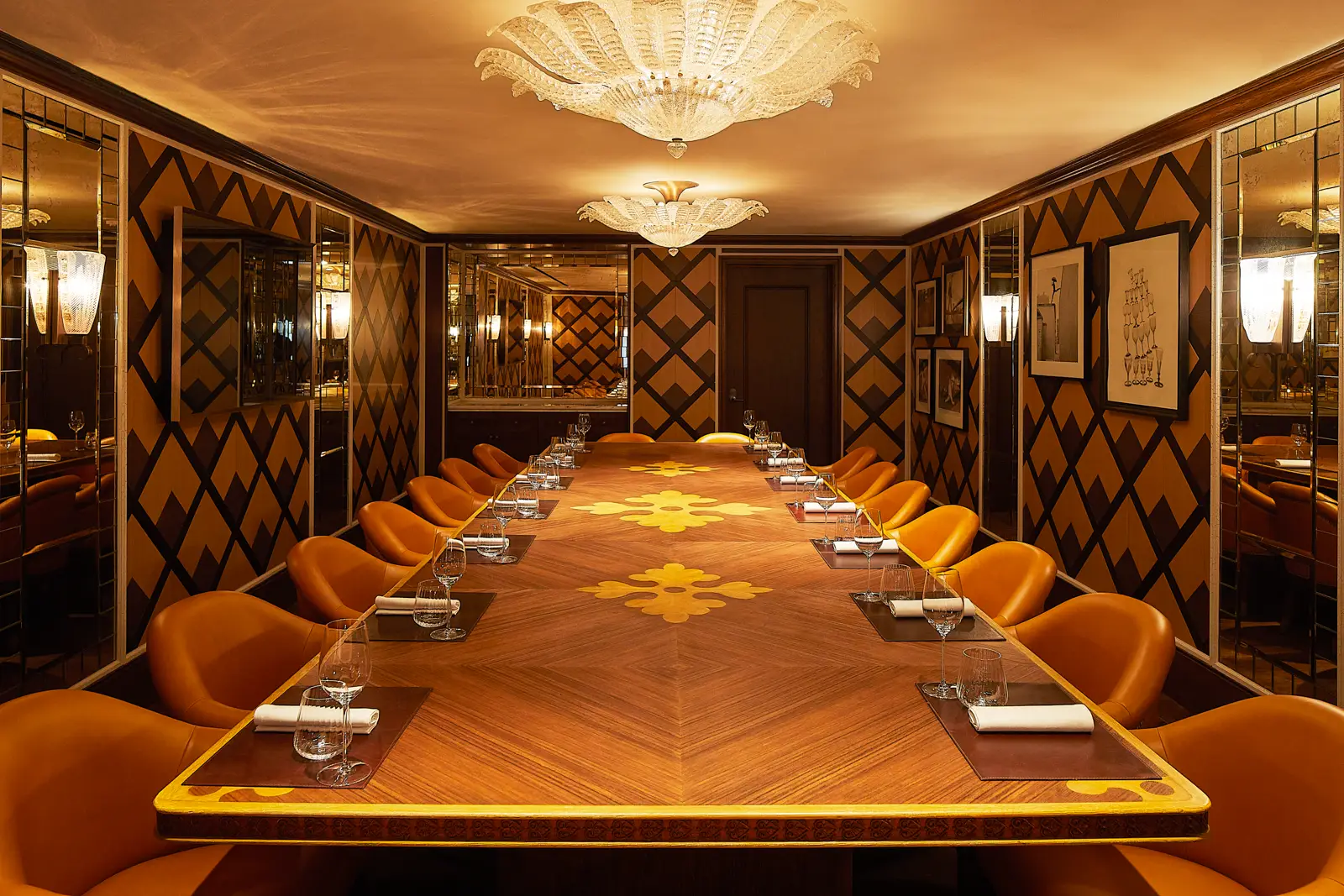 Elegant dining room with long wood table, orange chairs, mirrored walls, and chandeliers, set for a refined hotel gathering.