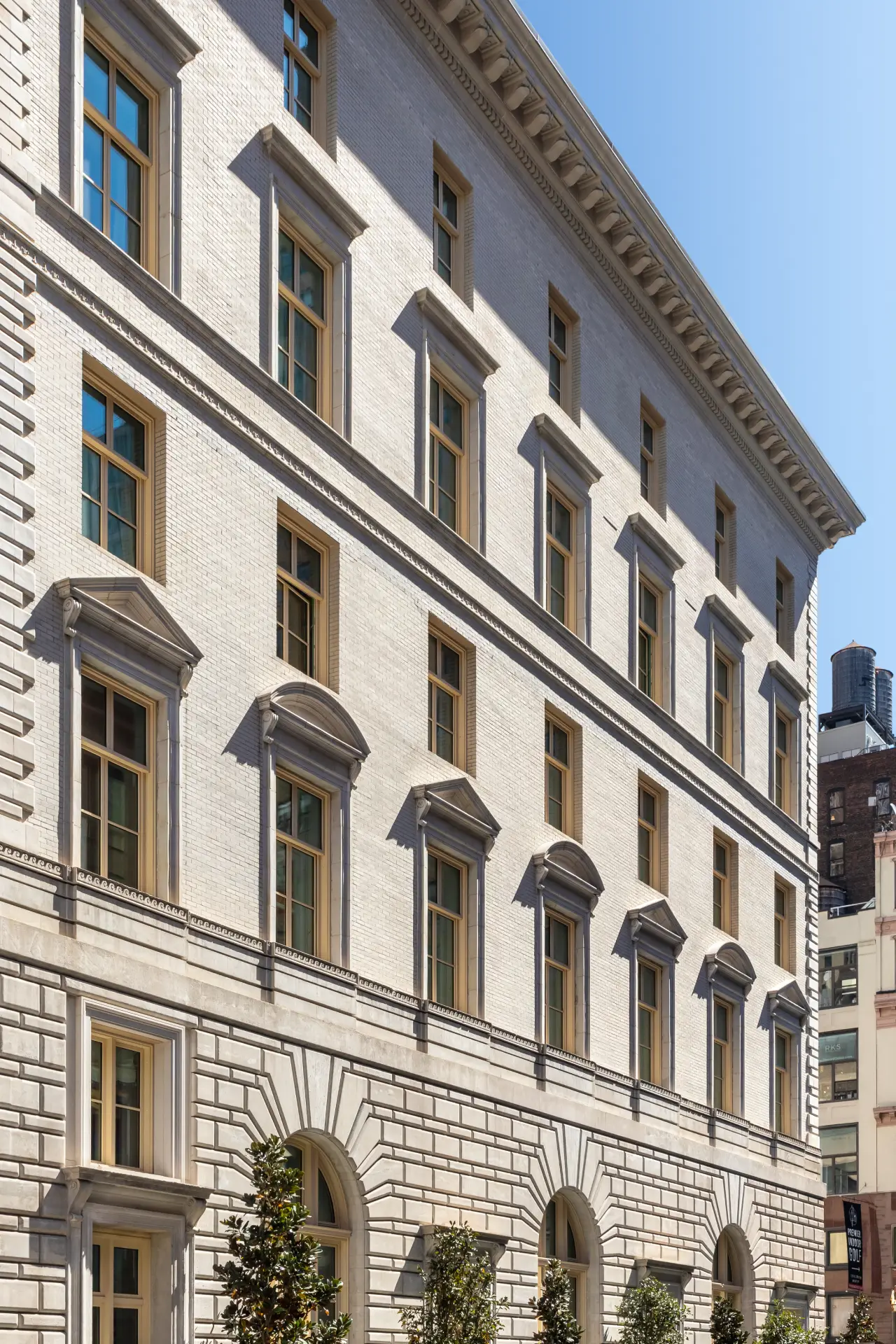 Building facade with arched and pedimented windows, ornate moldings, and textured stonework under clear blue sky.