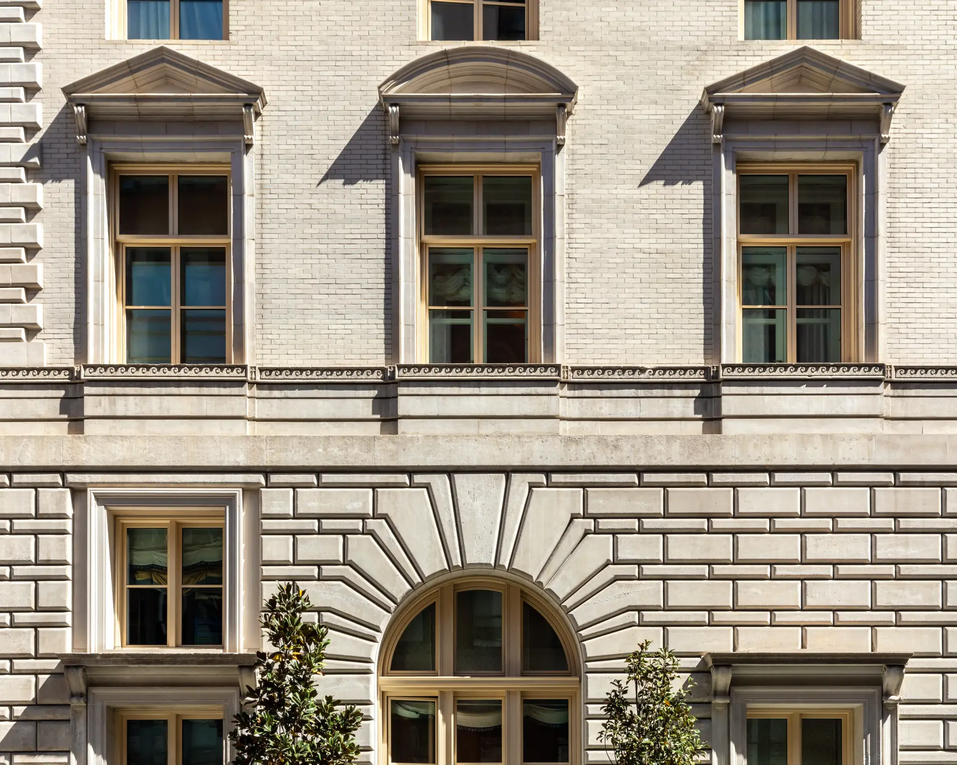 Classical building facade with arched and pedimented windows, light stone exterior, and elegant architectural detailing.
