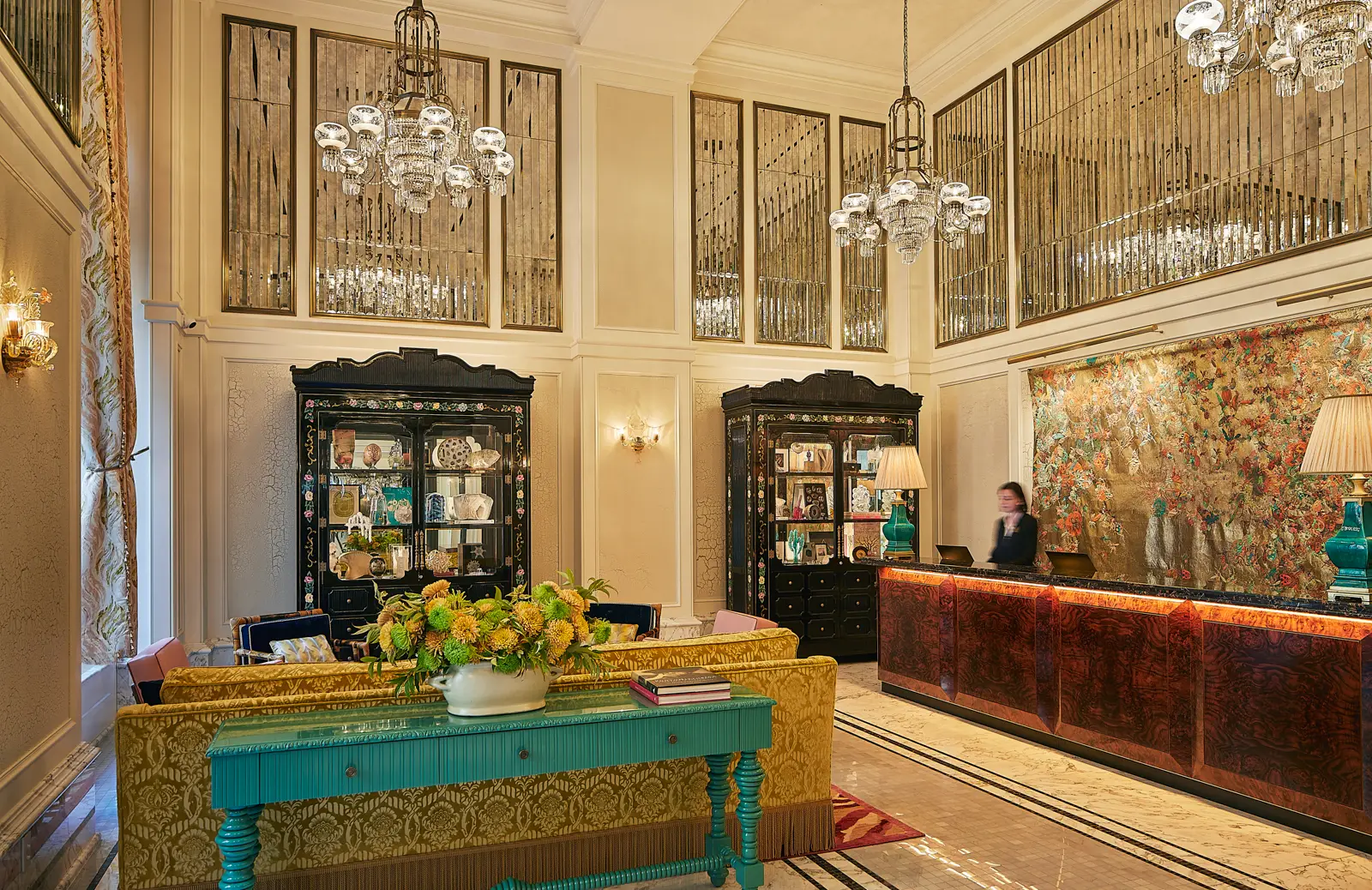 Elegant hotel lobby with high ceilings, ornate chandeliers, mirrored panels, plush seating, turquoise accents.