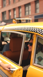 Yellow taxi with checkered trim and “OFF DUTY” sign, door open as person holds phone, passengers visible inside vehicle.