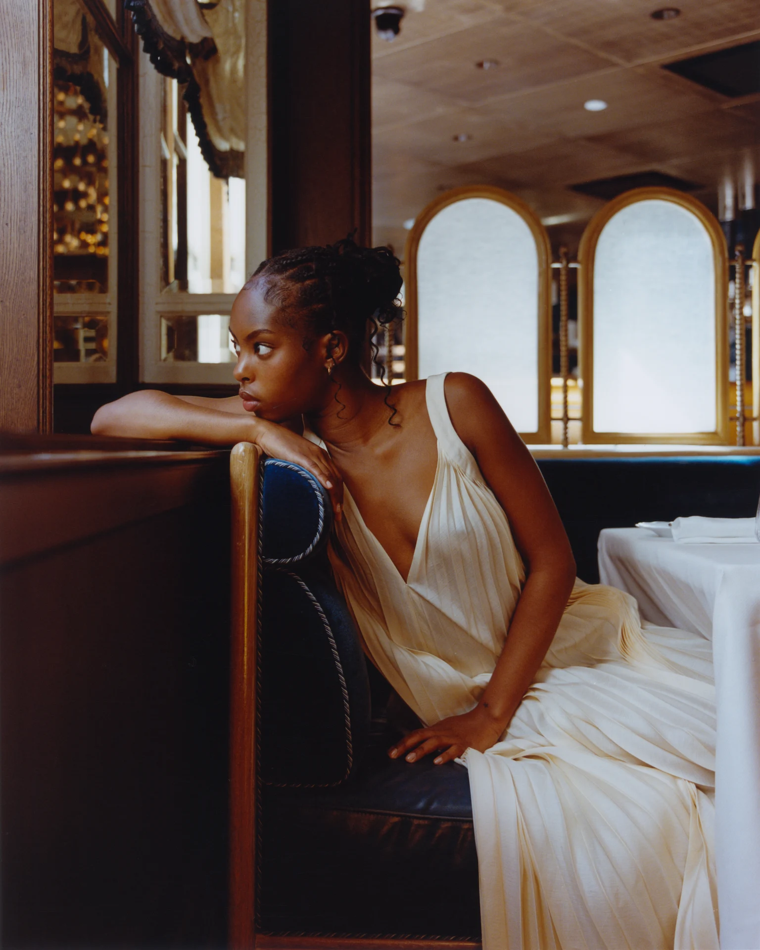 Person in flowing cream dress sitting in restaurant booth at The Fifth Avenue Hotel New York with wood paneling.