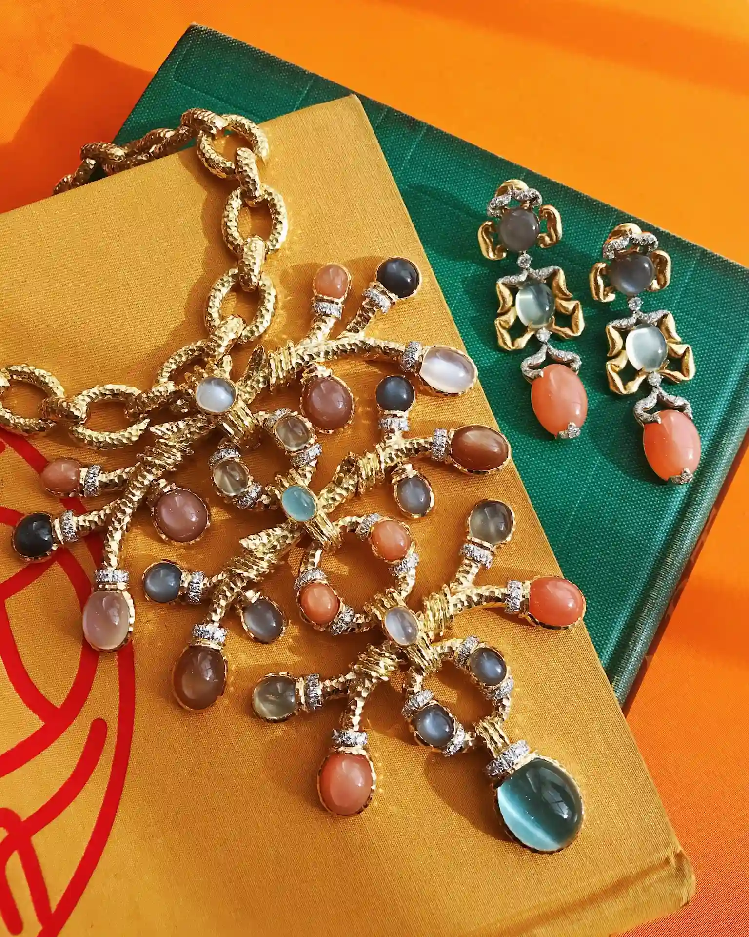 Colorful gemstone necklace and earrings displayed on books against vibrant orange background