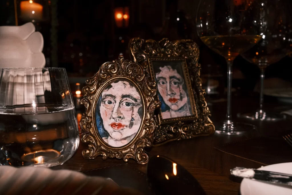 Close-up of elegant dining table with gold-framed miniature portraits, glassware, and warm candlelight.