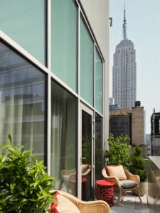 Urban terrace with wicker chairs, plants, and view of Empire State Building through glass reflections