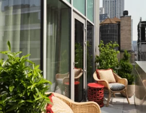 Urban terrace with wicker chairs, plants, and view of Empire State Building through glass reflections