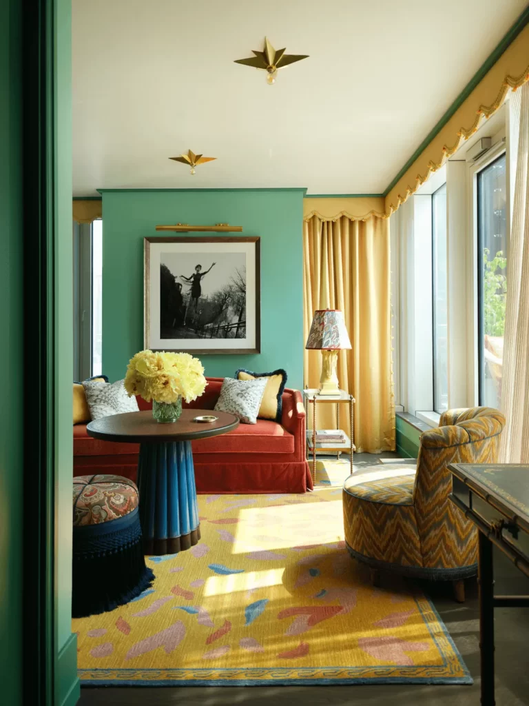 Eclectic living room with red velvet sofa, teal walls, gold accents, yellow rug, and artistic decor elements.