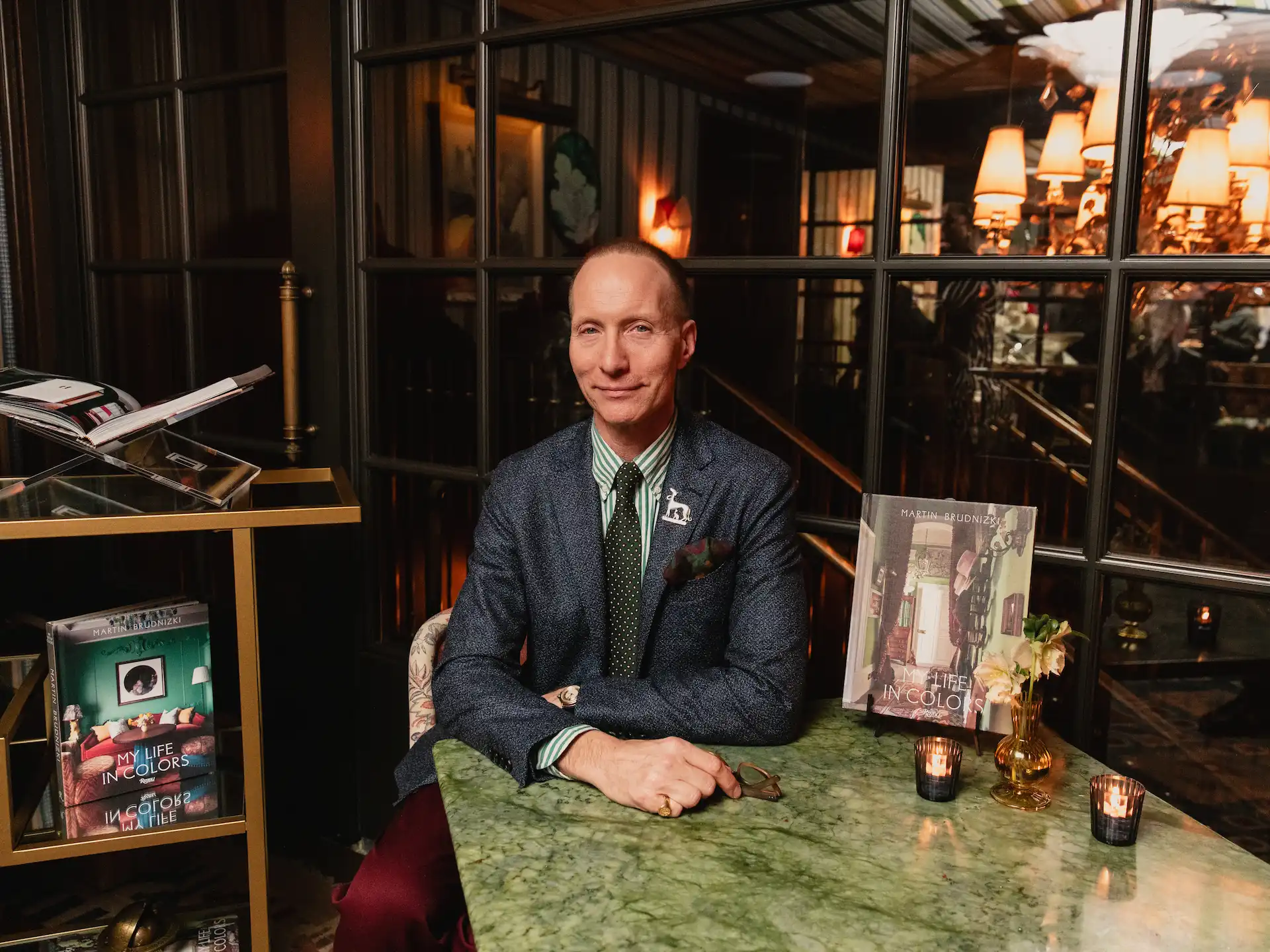Well-dressed person at green marble table with candles and book display in refined interior setting