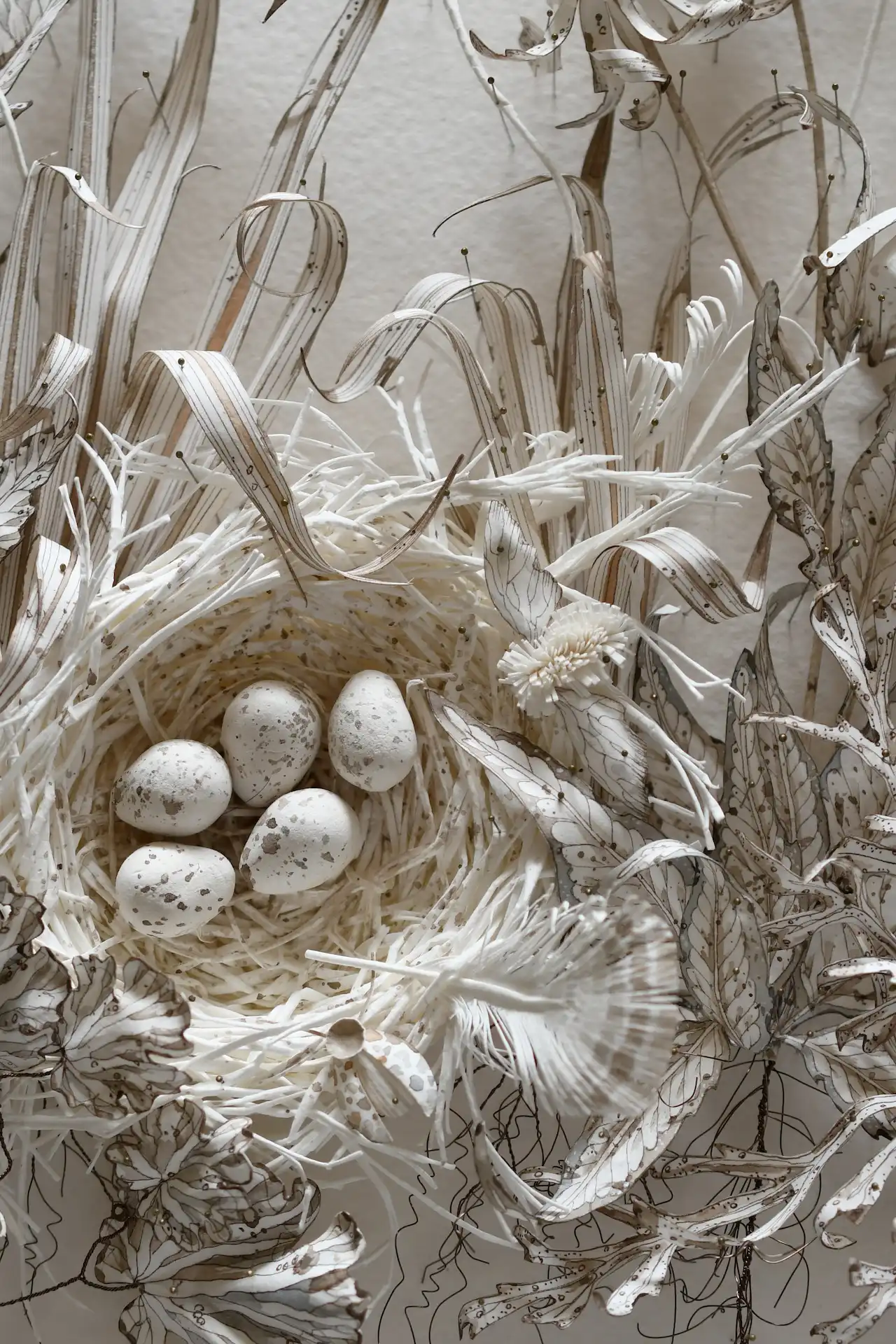 Bird’s nest made of fine straw surrounded by dried leaves, holding five speckled eggs in soft beige and light brown tones.