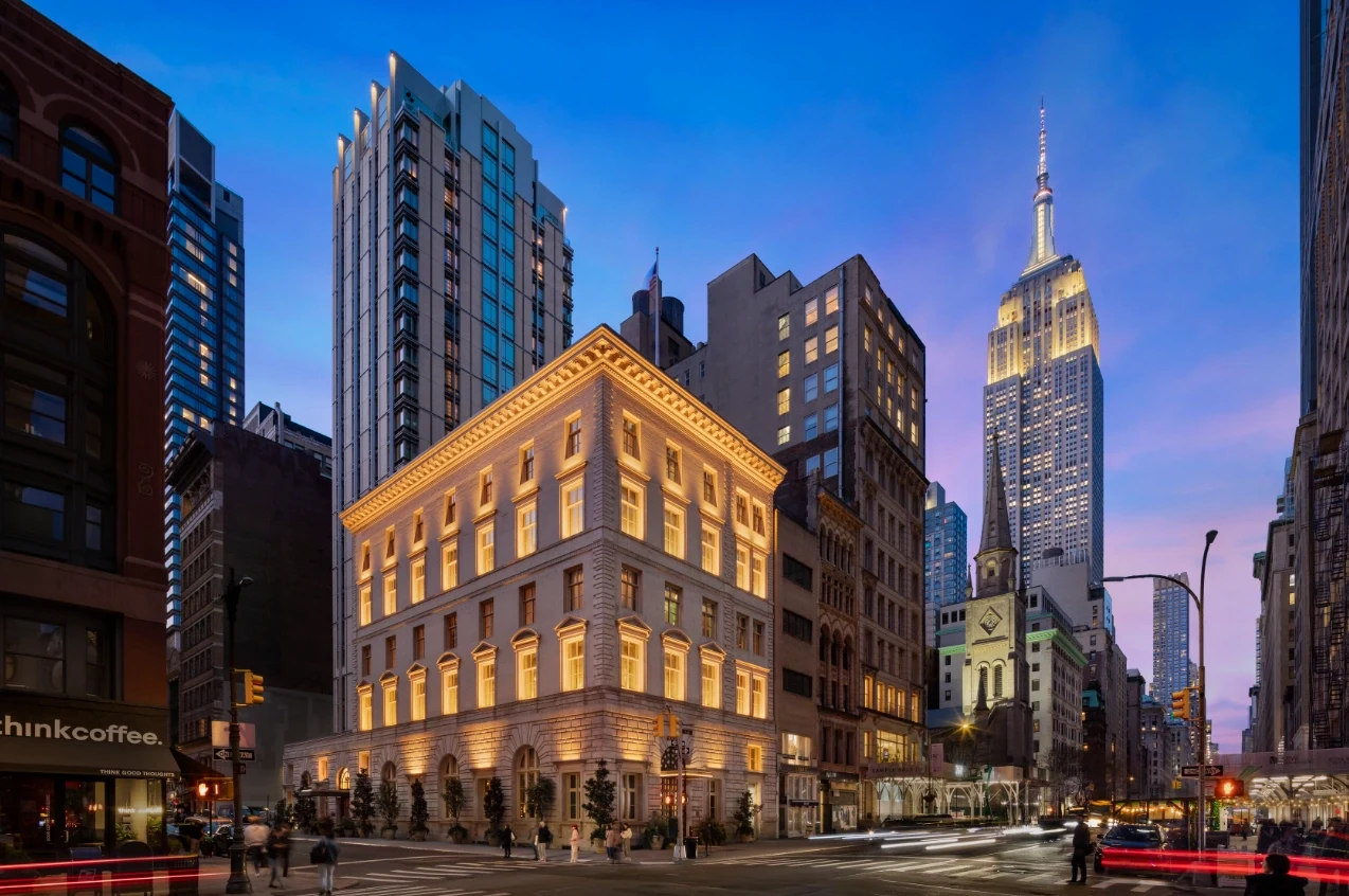 A photo of The Fifth Avenue Hotel brilliantly illuminated at night, surrounded by skyscrapers.