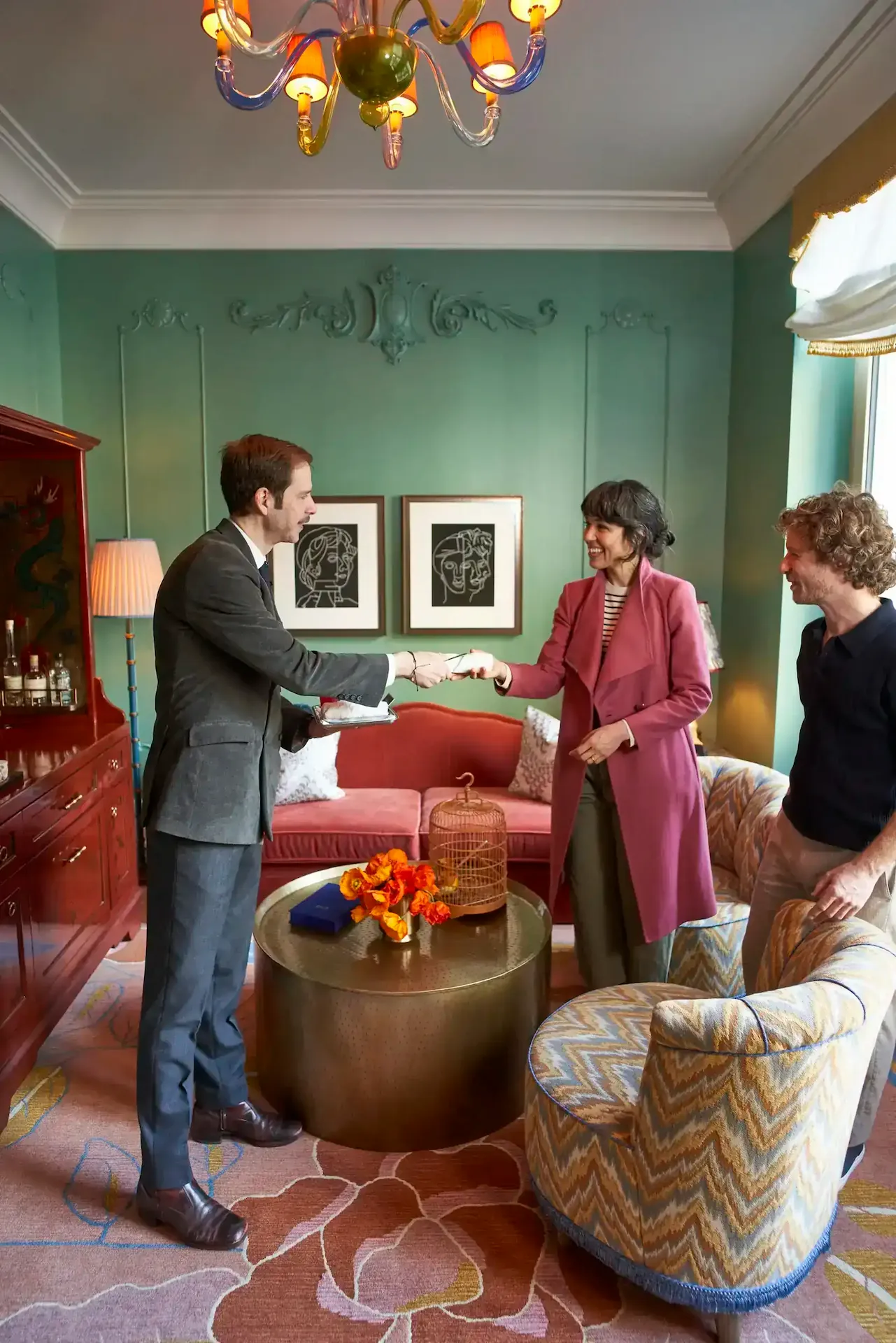 Two people smile while exchanging an item in a stylishly decorated room with green walls and modern art.