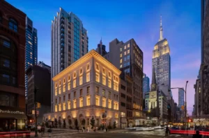 City street at dusk with the Empire State Building glowing above historic and modern buildings.