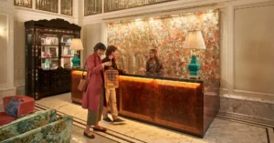 A lady at the counter welcomes a guest holding a birdcage.