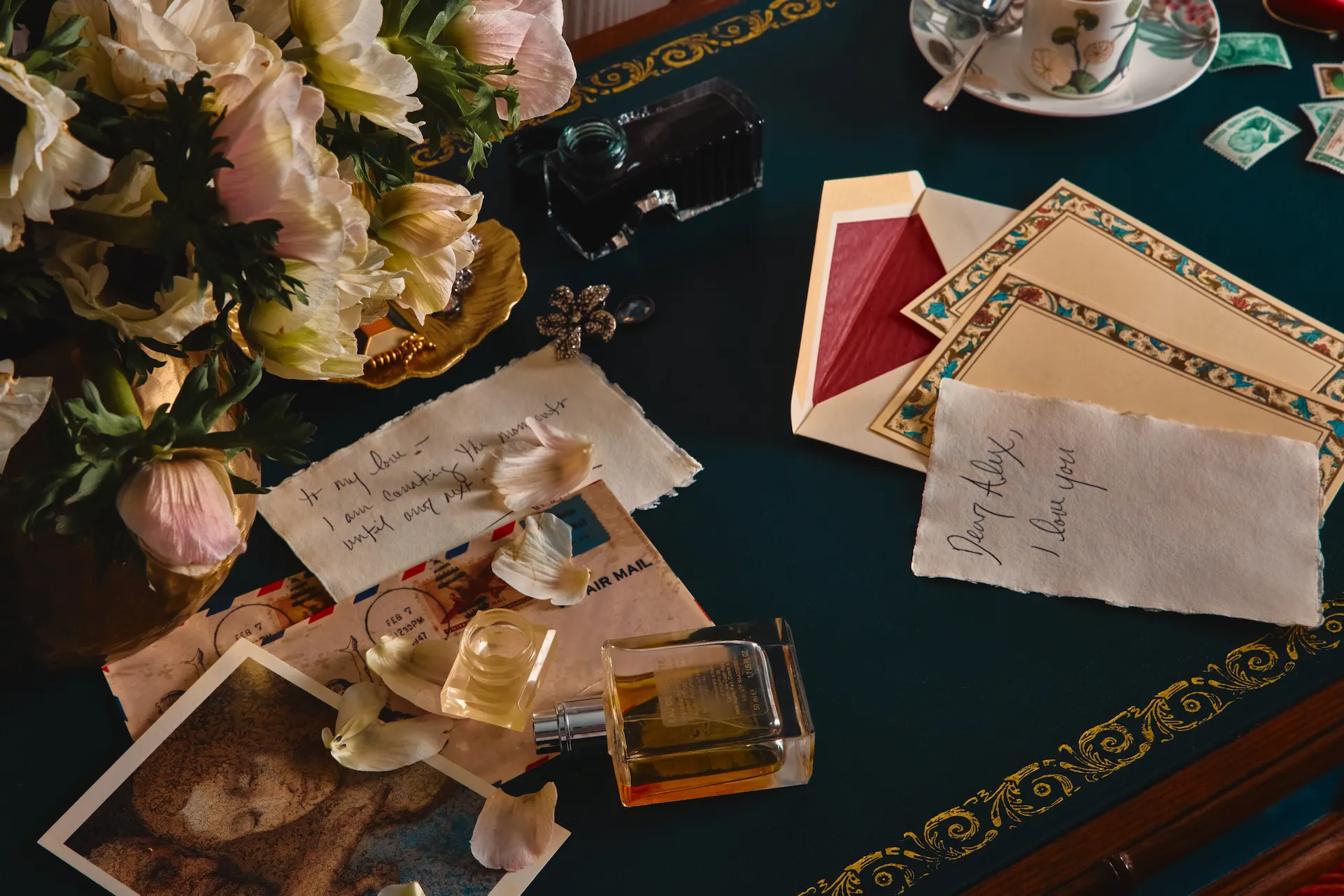 Vintage writing desk with flowers, letters, stamps, a teacup, and sentimental notes arranged decoratively.