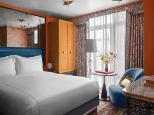 A well-arranged bedroom with a cozy bed, blue chair, and coffee table by the window.