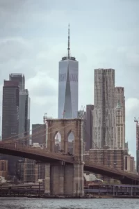 Brooklyn Bridge's stone tower framed against the Lower Manhattan skyline, with One World Trade Center's spire rising overhead