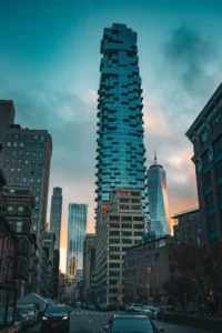 56 Leonard Street's stacked glass "Jenga" tower rising above Tribeca at dusk, with One World Trade Center glowing beside it under a teal sky