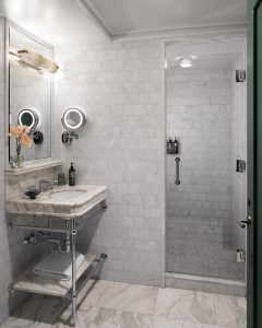 Luxurious marble bathroom with a double sink, illuminated round mirrors, and an adjacent glass-door shower.