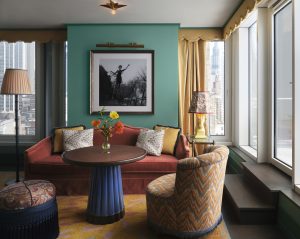 Teal accent wall with a framed black-and-white photo above an orange sofa; bright flowers on a round table in a sunlit living room.